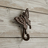 Cast iron butterfly wall hook with detailed wing cutouts and scrolled hook, rustic brown finish on whitewashed wood