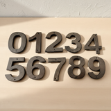 Overhead view of two sets of cast iron address numbers showing detailed metallic texture and dimensional relief