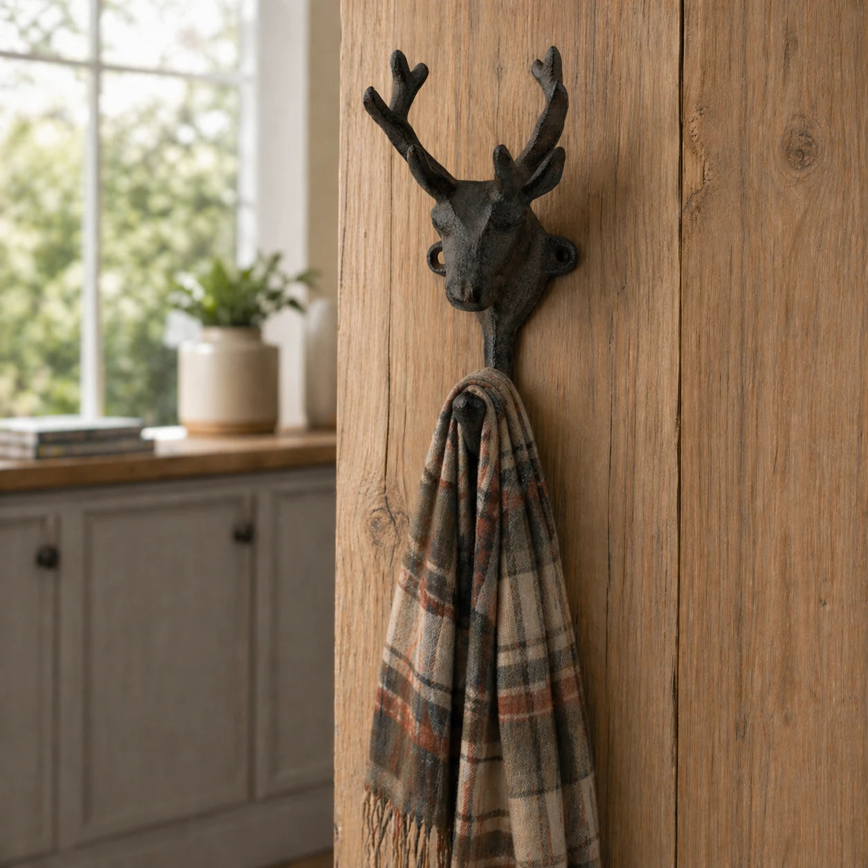 Cast iron deer head wall hook holding a plaid scarf.