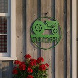 Bright green 21-inch vintage tractor welcome sign hanging on rustic wooden fence with red flowers below