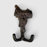 Rustic brown cast iron decorative saddle hook featuring detailed carved relief and curved lower hooks
