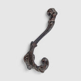 Rustic cast iron hook with decorative scrolled arms in aged finish for storage and decor