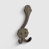 Antique cast iron decorative hook with dual prongs, weathered gray-brown rustic finish