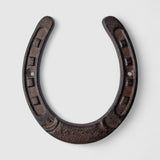 Large cast iron horseshoe with decorative stamped details, aged dark finish on blue shiplap
