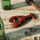 Red cast iron lobster bottle opener with detailed claws and segmented body on driftwood