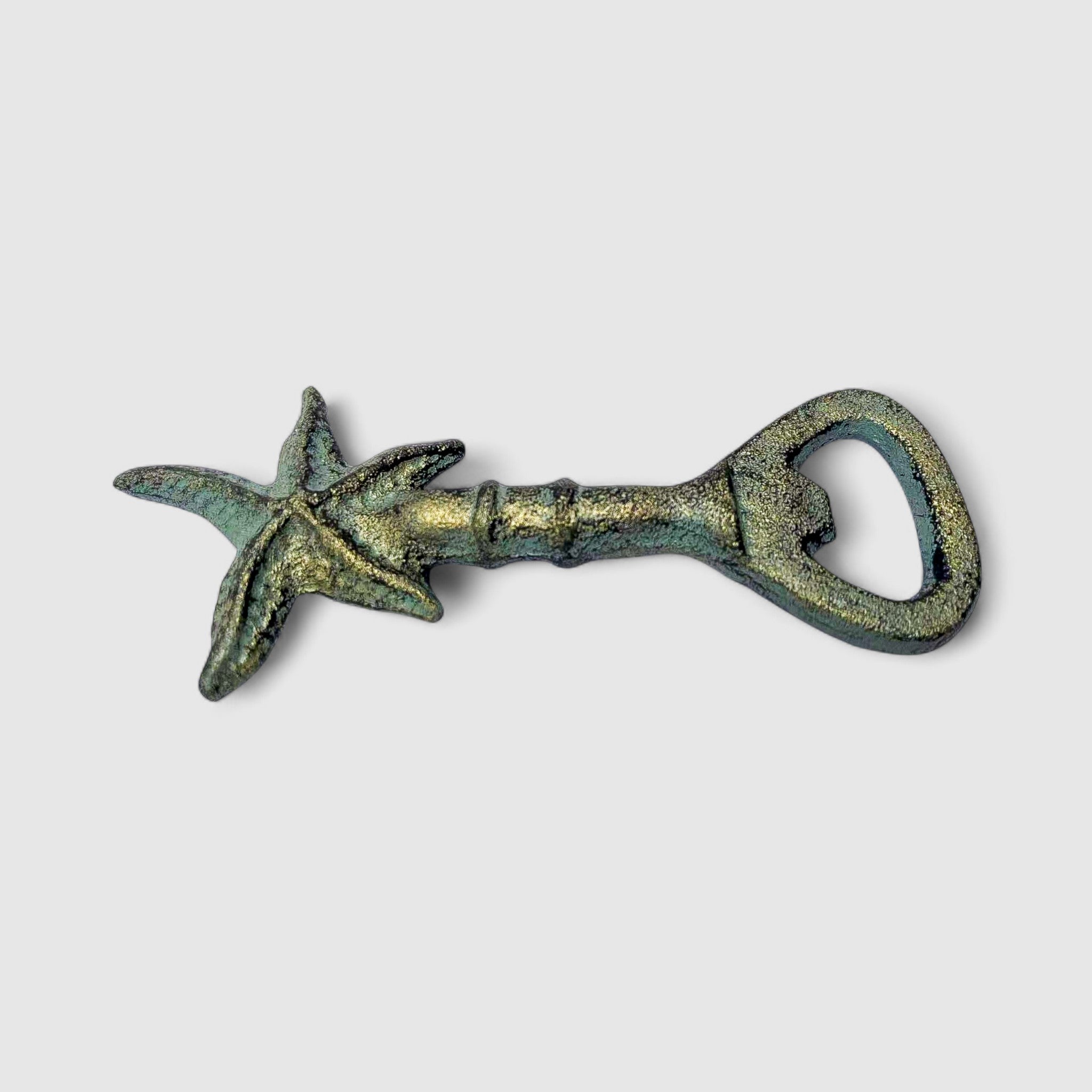 Green patina cast iron starfish bottle opener displayed on sand with driftwood, coastal styling