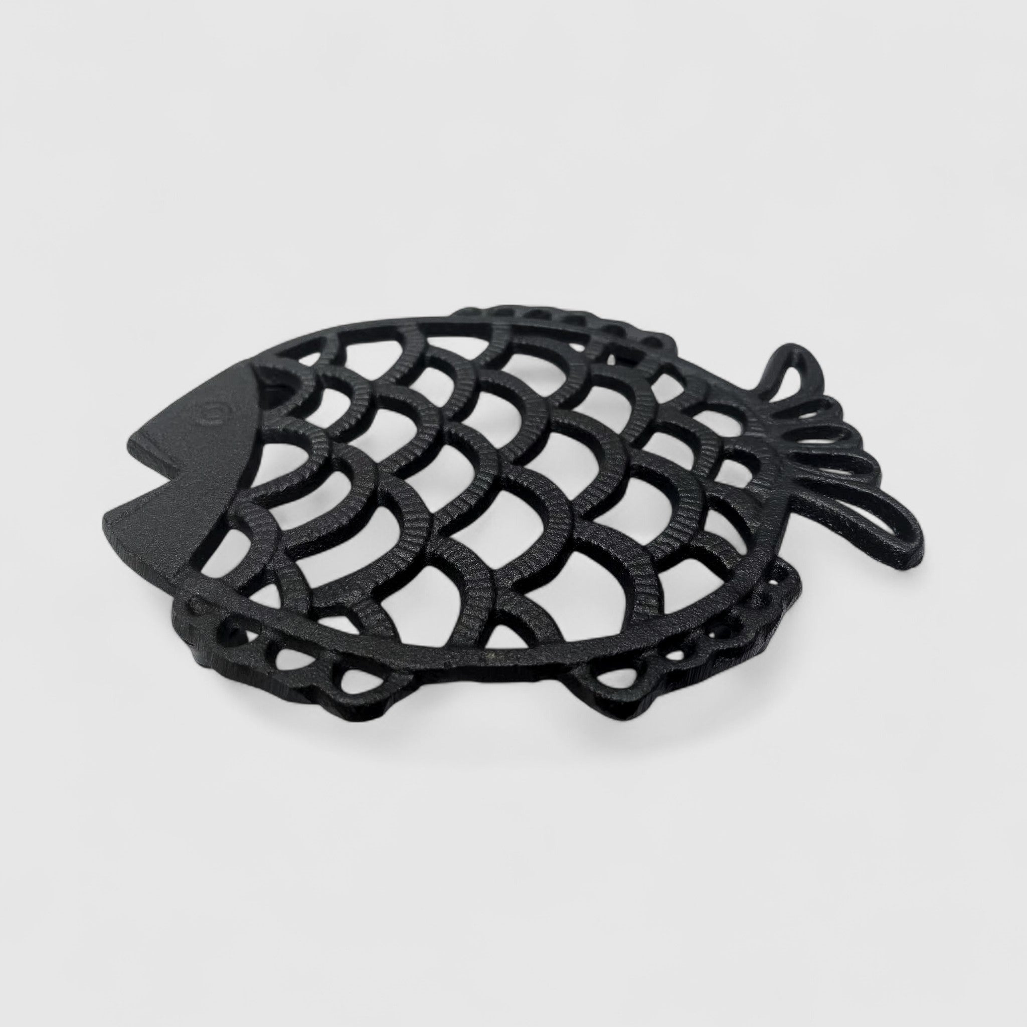 Angled top view dark cast iron fish trivet with openwork scale design and draped tail