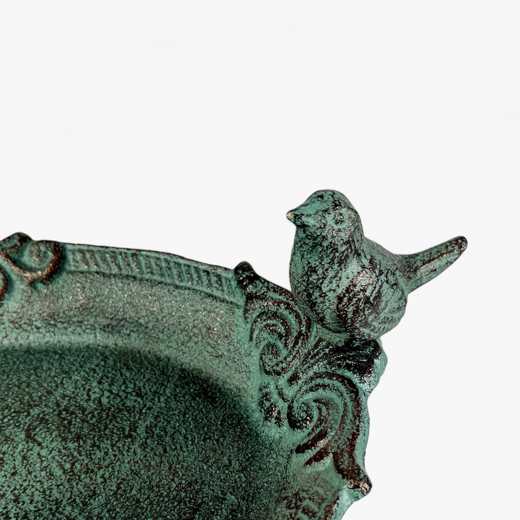 Close-up of cast iron bird bath rim with ornate scrollwork design and green patina finish bird sculpture