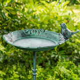 Cast iron bird bath bowl detail showing green verdigris patina, scrollwork trim, and ceramic bird perch