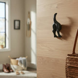 Black cast iron dog tail wall hook mounted on light wood wall, rustic home decor