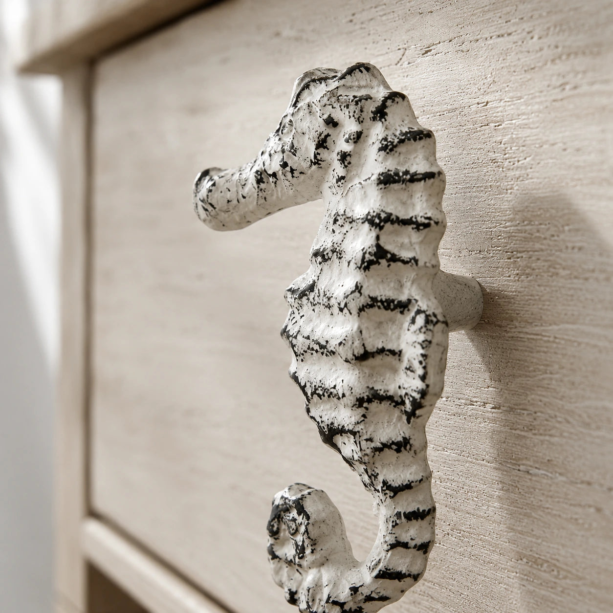 Close-up of distressed white seahorse drawer knob on a textured cabinet front