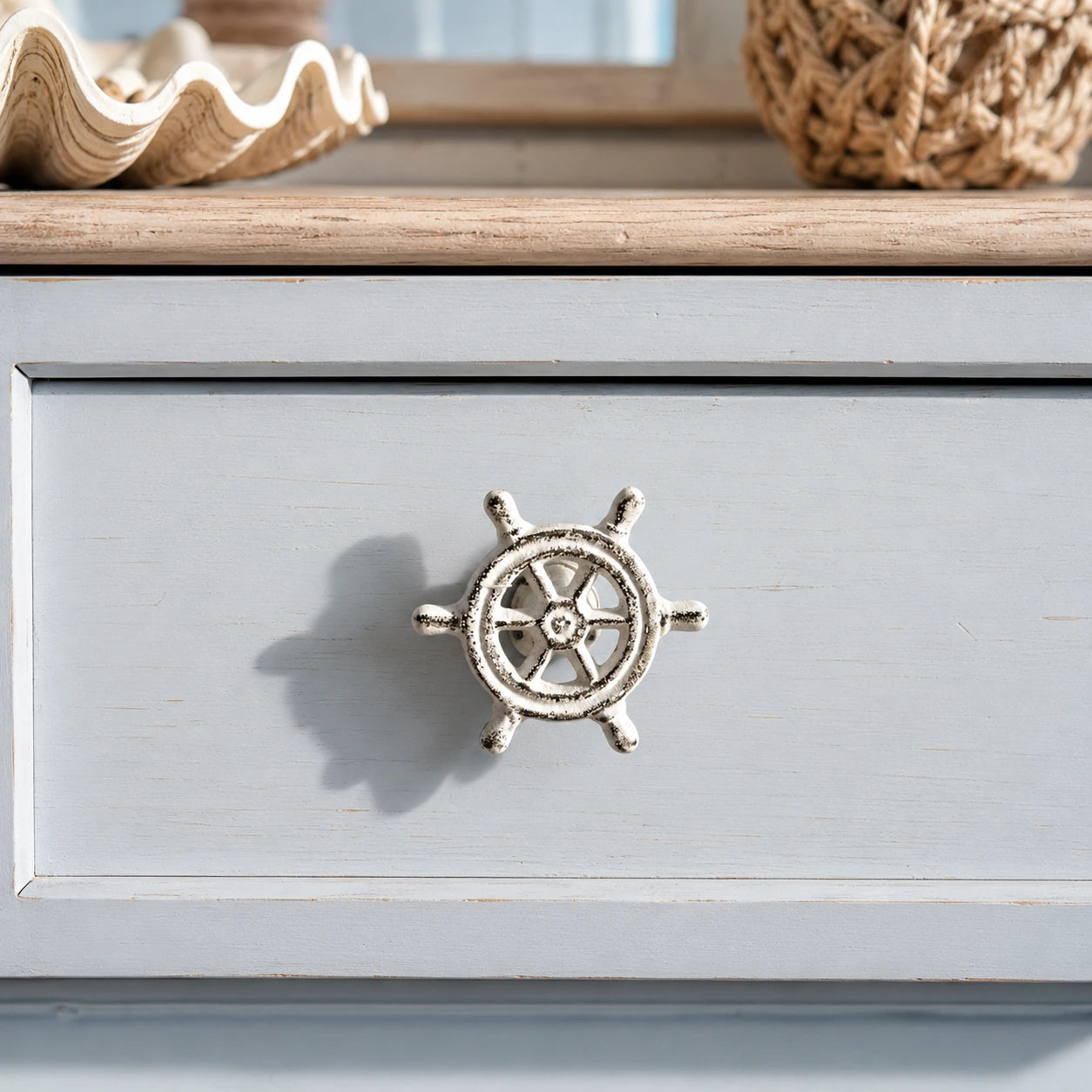 Distressed white ship wheel cabinet knob on a pale blue coastal dresser drawer