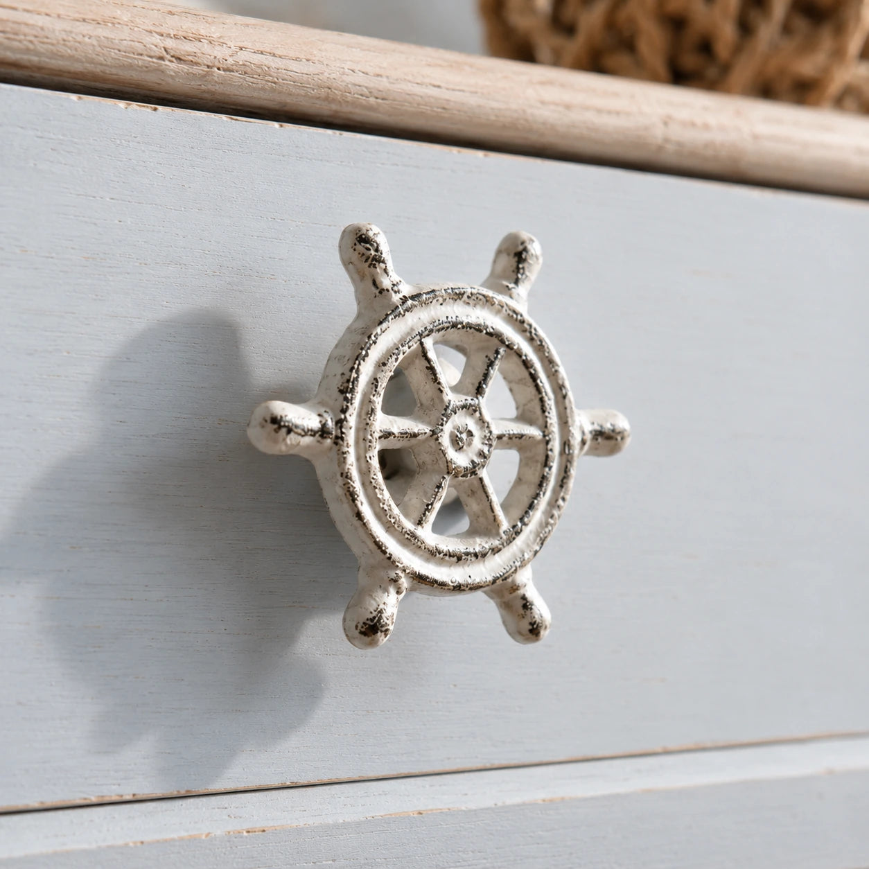 Close-up of distressed white ship wheel drawer knob on a light blue cabinet front