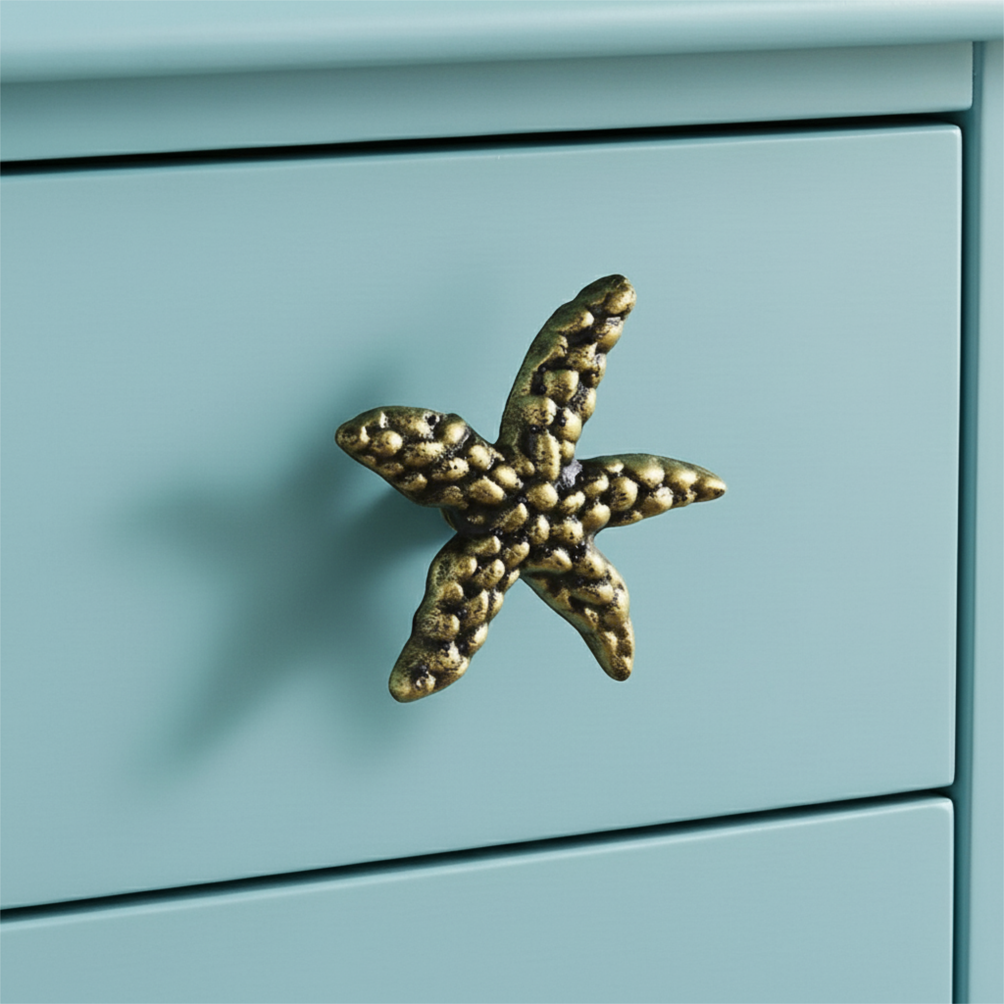 Weathered brass starfish cabinet knob on blue drawer, coastal hardware detail