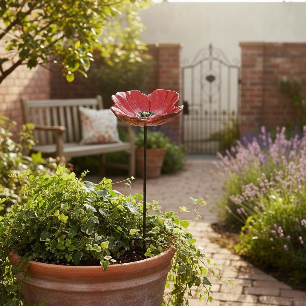 Red poppy cast iron garden stake bird feeder with yellow center, in terracotta pot with foliage