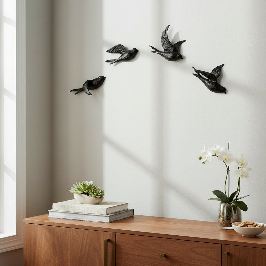 Set of four black cast iron bird wall hooks displayed on white wall above wooden cabinet with plants and books