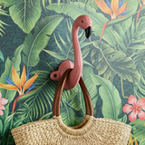 Pink flamingo wall hook with a woven bag on a tropical leaf background