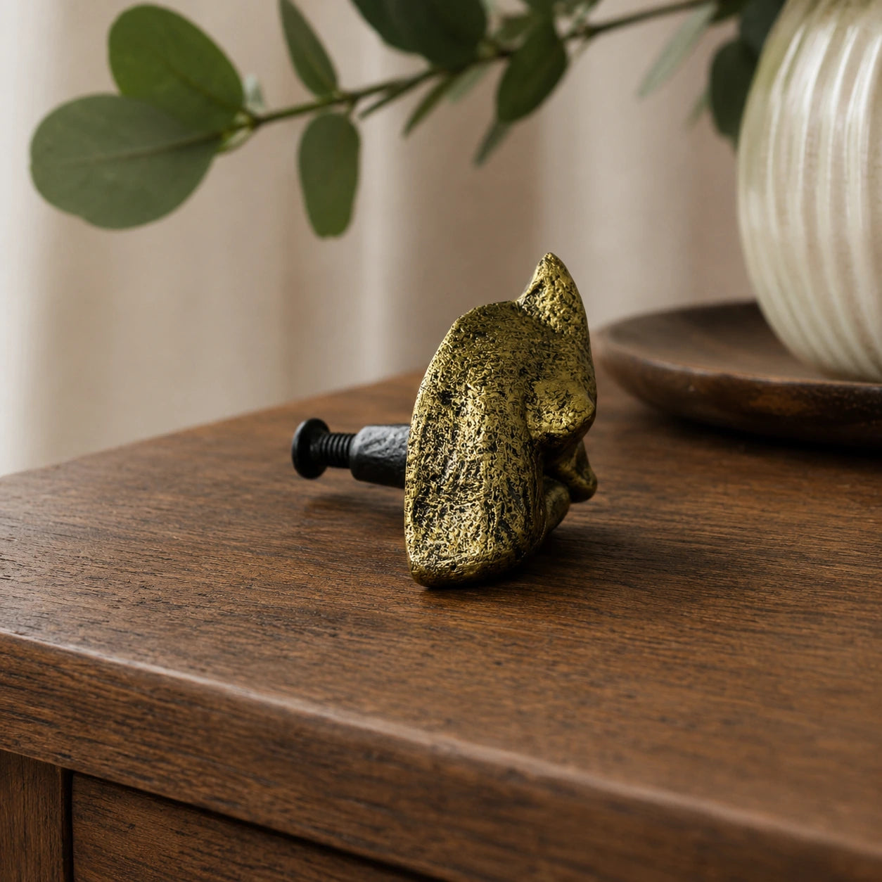Side view of antique brass fox cabinet knob with mounting screw on wood tabletop