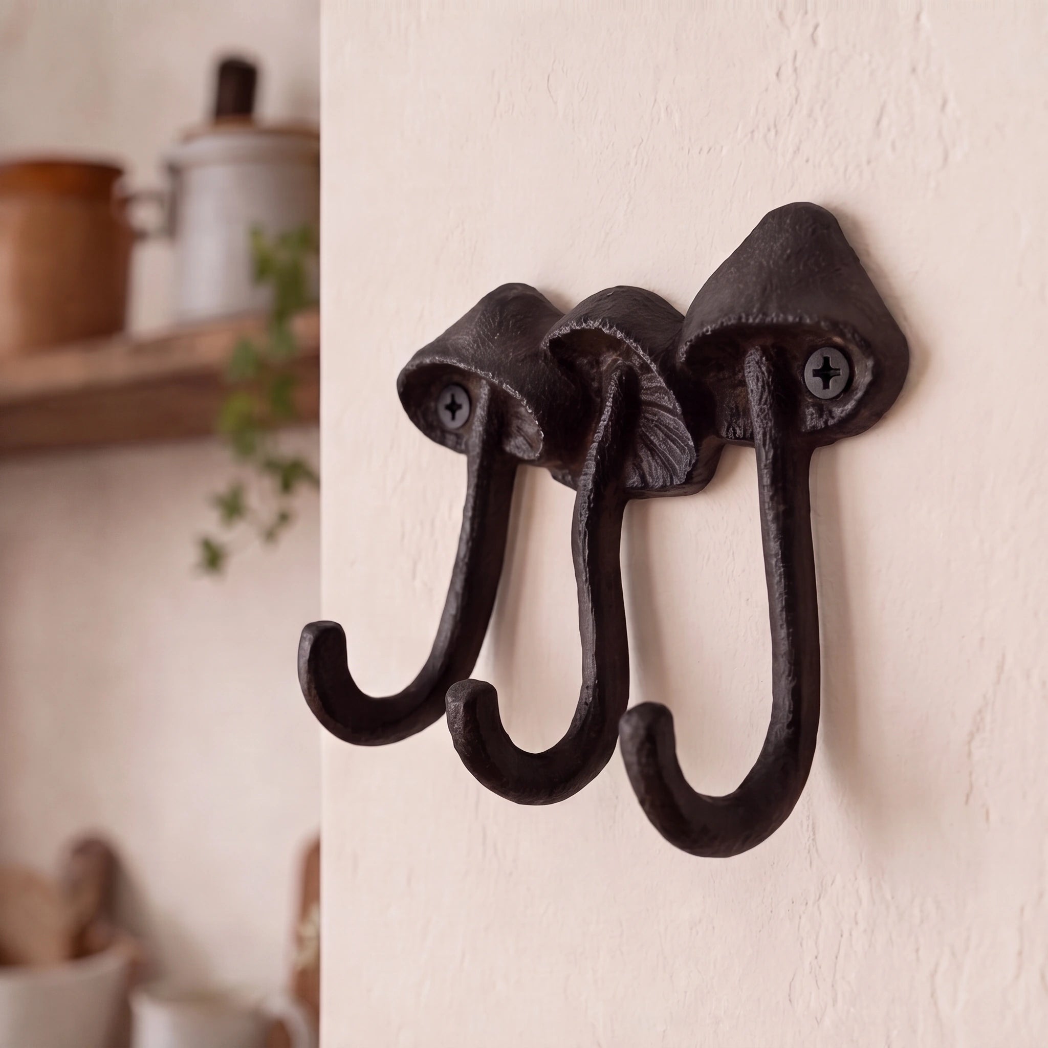 Close angled view of dark black-brown cast iron mushroom wall hooks with three curved hooks, SKU GB78067